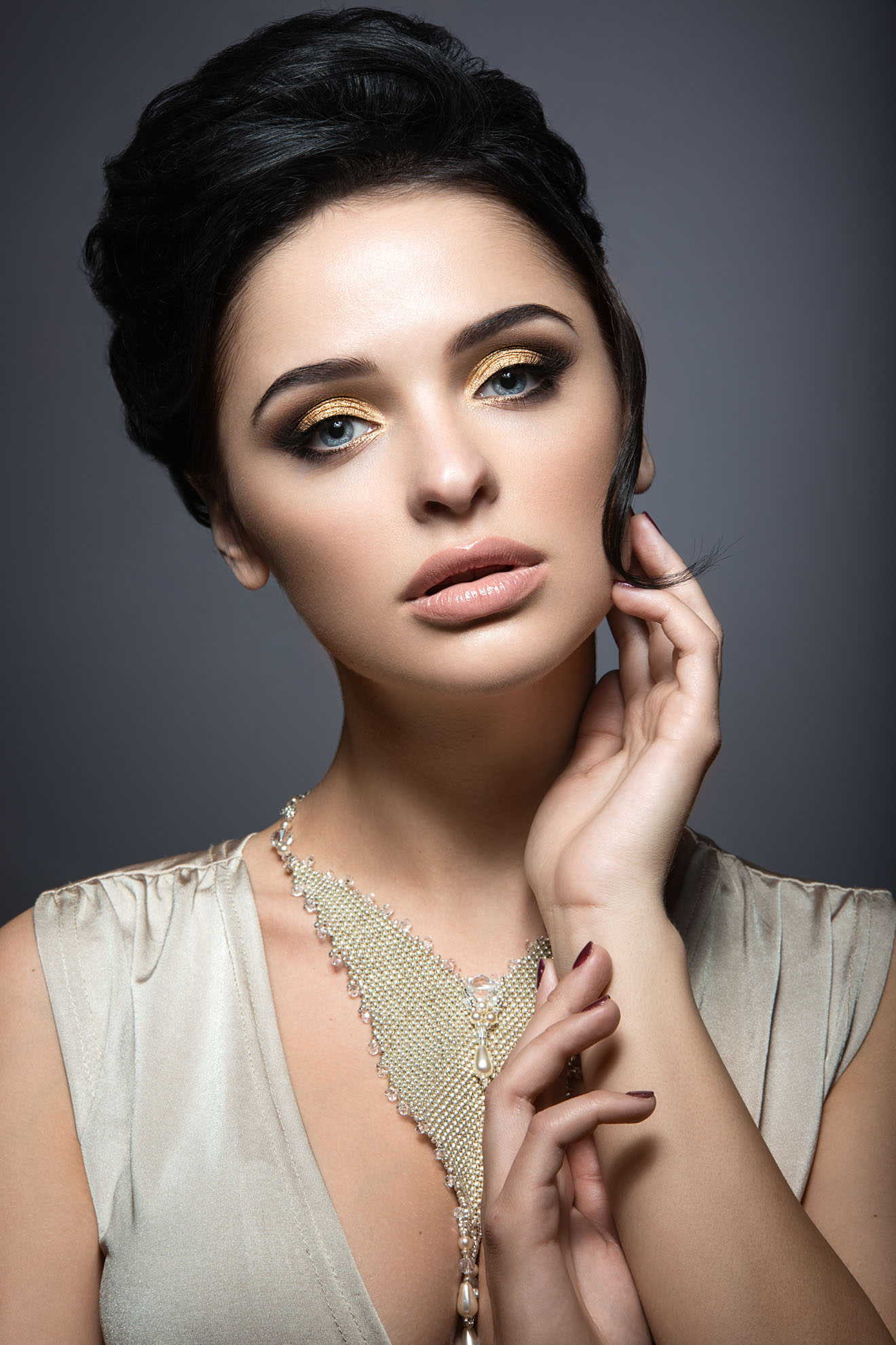 Beautiful brunette woman with perfect skin, gold makeup and handmade jewelry. Beauty face. Picture taken in the studio on a grey background